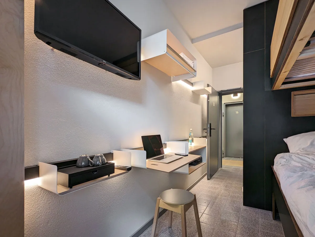 Schmales Zimmer mit Fernseher, beleuchteten Ablagen und Klapptisch